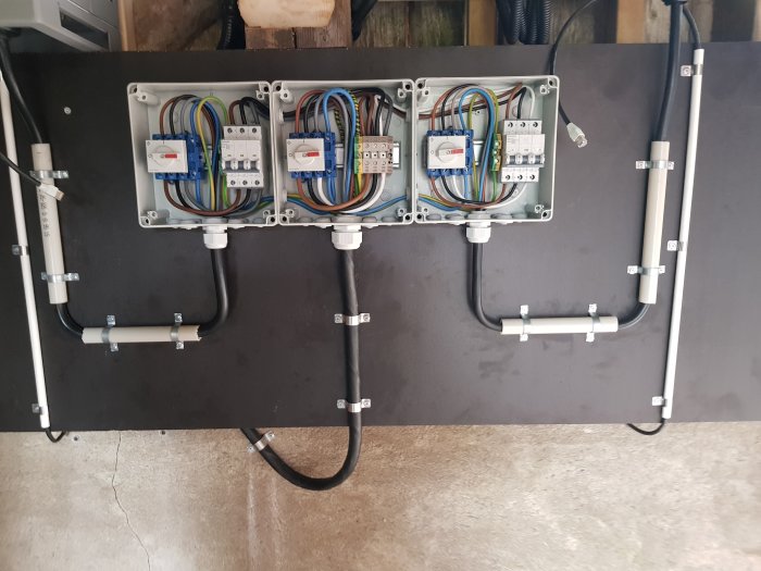 Elektriskt installationsskåp med kablage, säkringar och omkopplare för solcellsproduktion, ordnat och monterat på en svart bakgrund.
