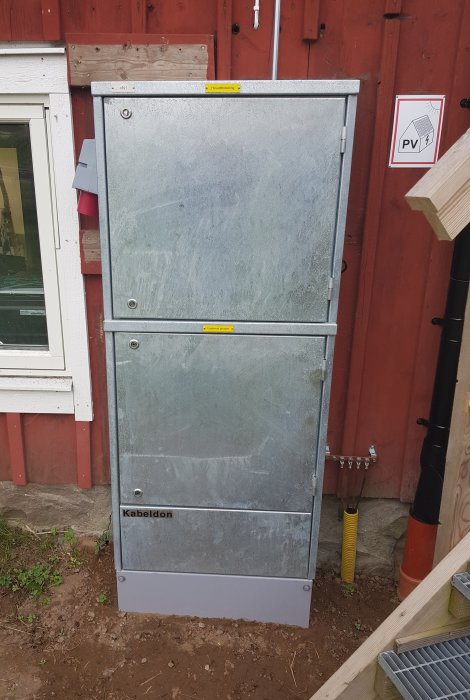 Ett grått elskåp för solcellsanläggning med varningsmärkningar för PV-system och Jordfelsbrytare, märkt "Kabeldon".
