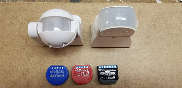 Två PIR-sensorer av olika modeller och tre automationsenheter på träbänk.
