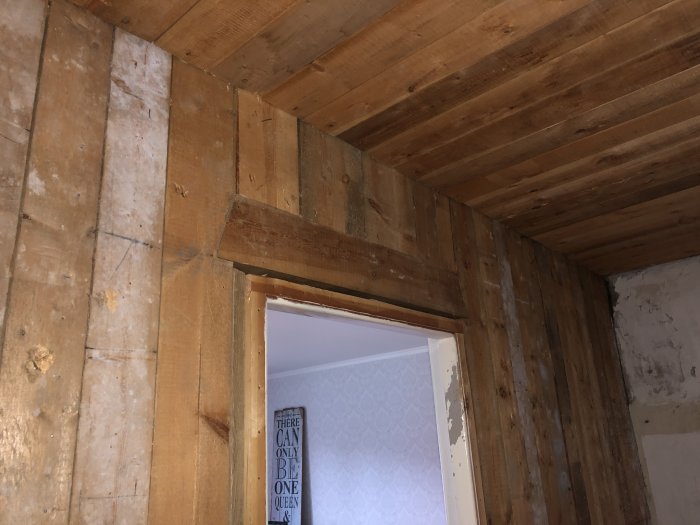 Innvendig trevegg med døråpning, laget av kraftige tretavler, på et oppussingsprosjekt. Tydelige merker og slitasje på overflaten.