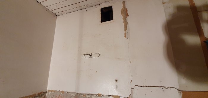 Vägg under renovering med ojämnt borttaget kakel och synlig spjällring.