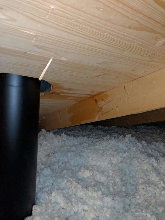 Vattenläckage på vinden med isolering och träbjälkar synliga, nära en svart skorsten.