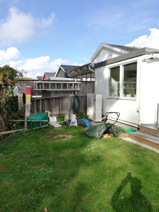 Hörna av trädgården med gräs och ojämn mark, intill ett hus med fönster, redo för att bli en grillplats.