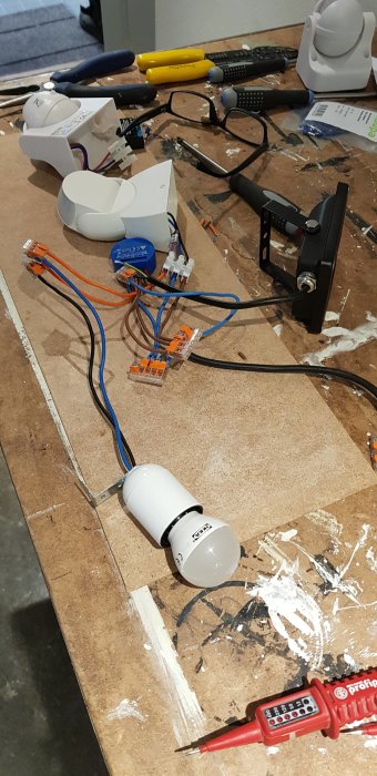 Elektriskt experiment med sensor, LED-lampor, kopplingsklämmor och verktyg på en plywoodskiva.