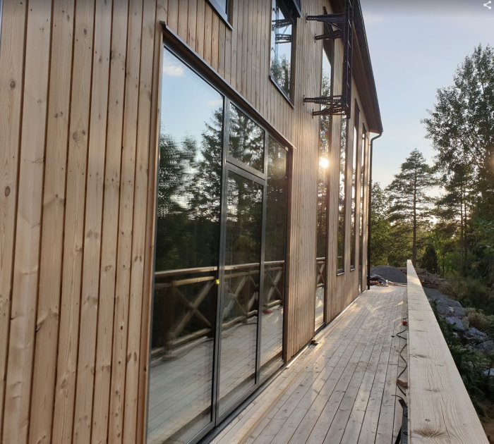 Thermowood-fasad på hus med reflekterande fönster och träterrass i solnedgång.