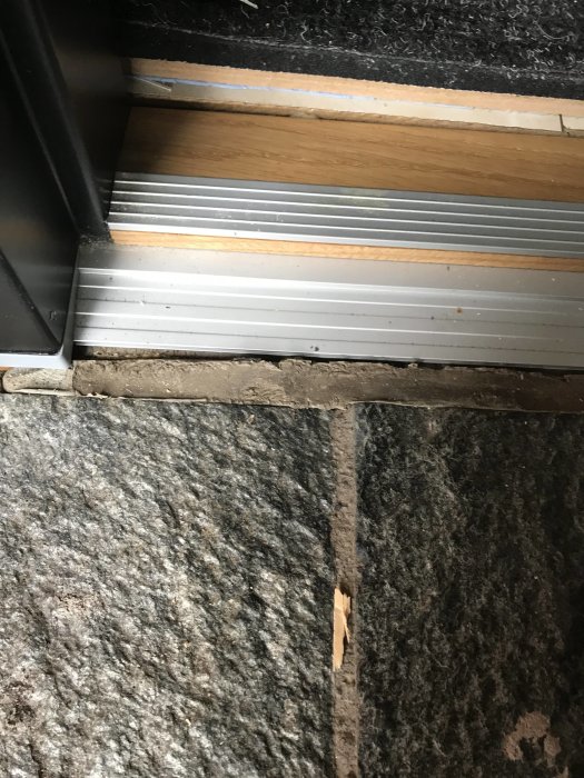 Tröskel till ytterdörr med synlig fog mellan klinker och dörrtröskel som behöver bytas.