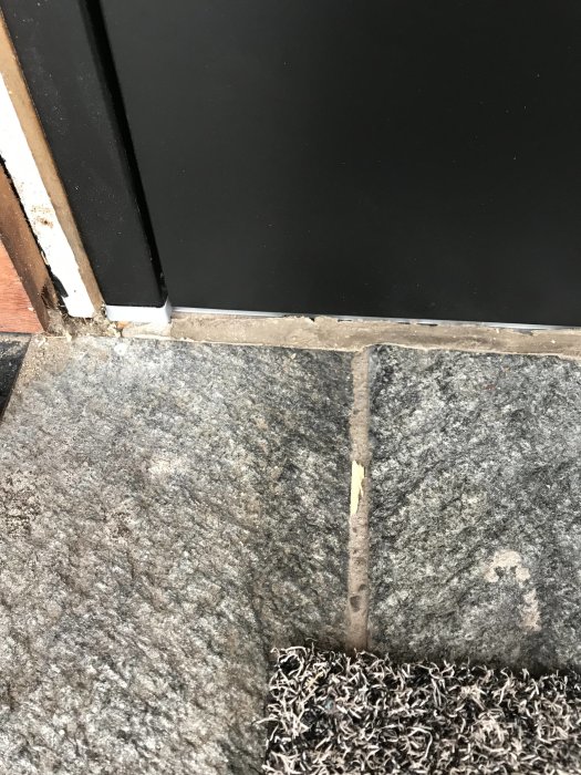 Ytterdörr som möter en klinkertröskel med synlig fog som behöver bytas och grå klinkerplattor.