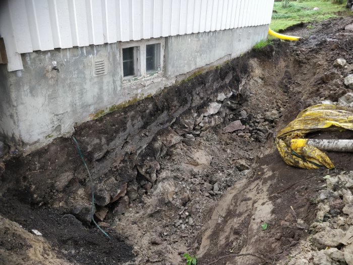 Grunden till ett hus med synligt skadat och ojämnt underlag och lösa stenar, planerar för stödmursgjutning.