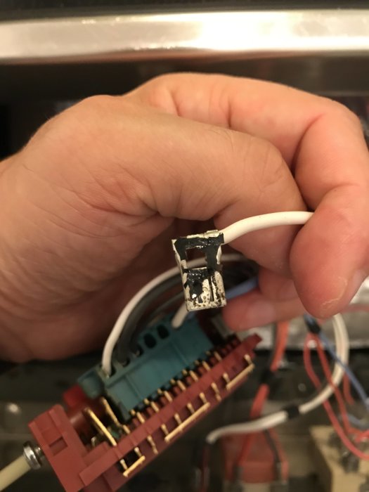 Närbild på en hand som håller en vit elektrisk kabel med smält plast och skadat kontaktstycke.