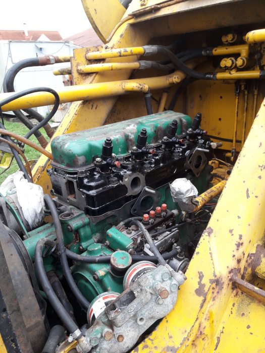 Monterad topp på en maskinmotor med gula och gröna delar, synliga rör och kablar, ej färdigställd.