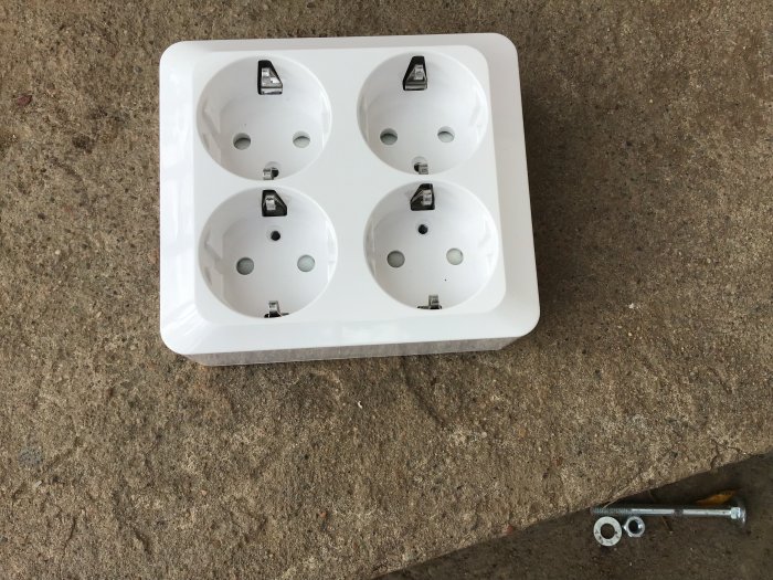 Schneider Exxakt 4-vägs eluttag liggande på betong med skruvad framsida och löstagbara skruvar vid sidan.