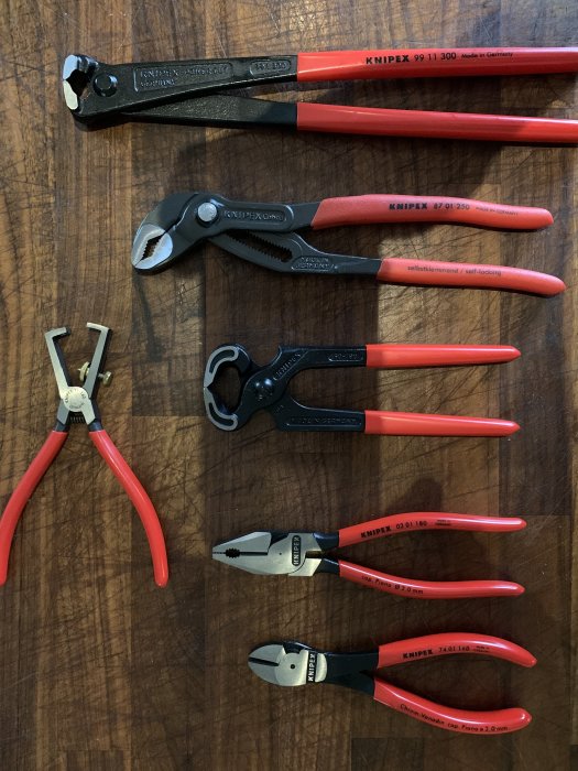 Ett sortiment av Knipex verktyg inklusive en hovtång, Cobratång och avbitartång med röda handtag på träbakgrund.