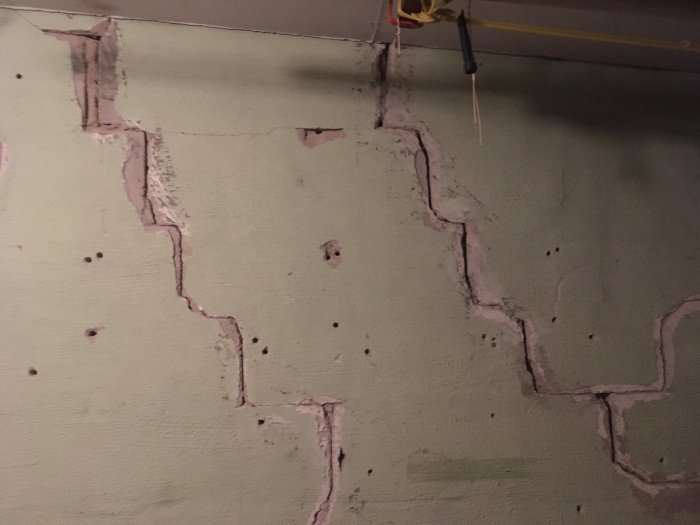 Sprukket vegg av lettbetong med mange dype sprekker og flere små skruvhull.