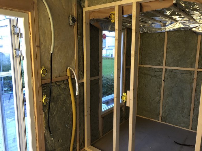 Renoveringsprojekt med isolering i väggar och tak, synliga trästommar och elinstallationer i ett ofärdigt rum.