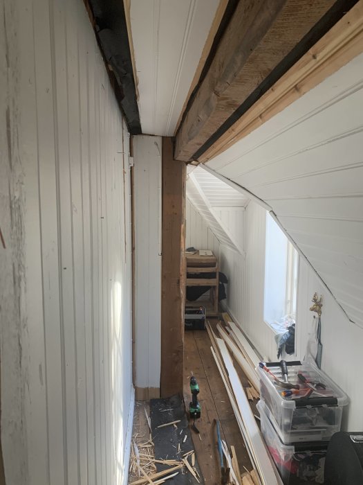 Kattvind med vit plankvägg nära en takstol och verktyg på golvet, indikerar pågående rivningsarbete.