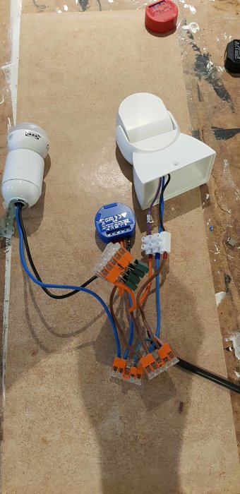 Elektroniskt testupplägg med kondensatorer och ledningar på en träskiva, inklusive Shelly smart-relämodul.