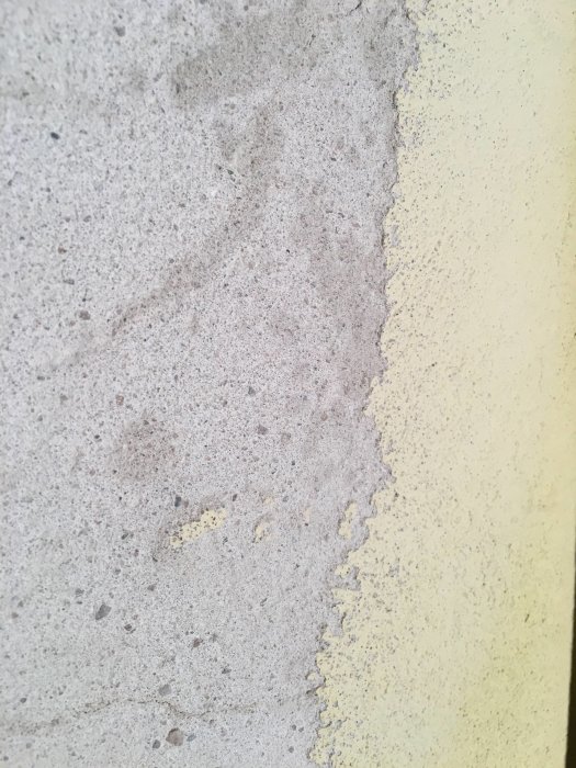 Ojämn vägg där en del av färglagret slipats bort, visar 1mm tjockt färglager och rå betong.