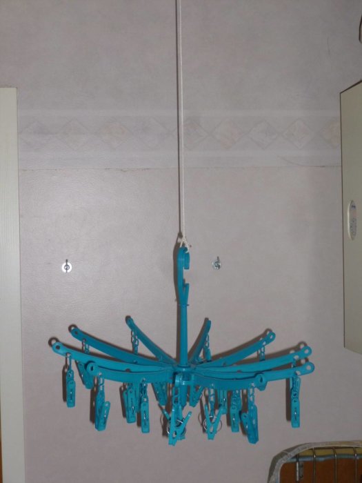 Blå tvättklämmor på en roterande torksnurra hängande från taket i ett rum.