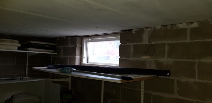 Oinredd källare med exponerad betongblocksvägg och ett litet fönster, behöver renovering för att bli sovrum.