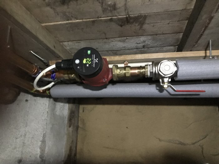 Vattenpump kopplad till vattenburna elementsystemet, insatt i isolerad rörledning, med mätdisplay och röd regleringsventil.