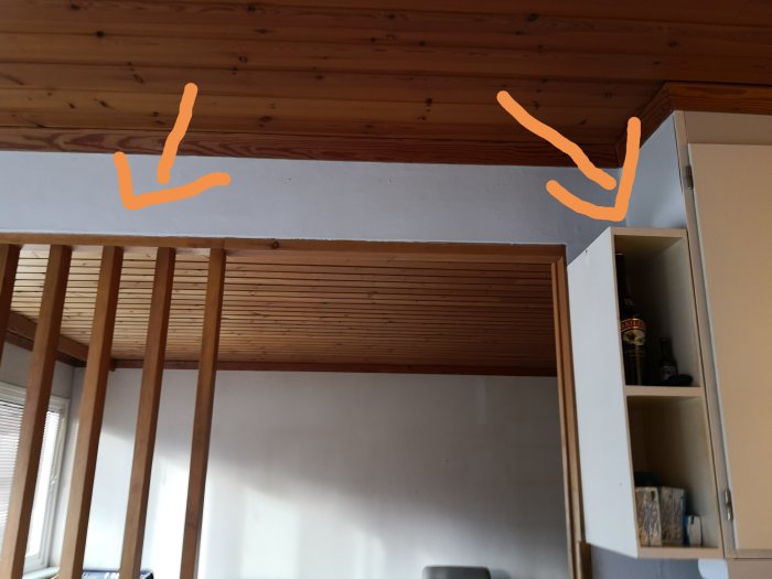 Vy av en vägg mellan kök och vardagsrum med en träbjälklagstak och en delvis öppen vägg.