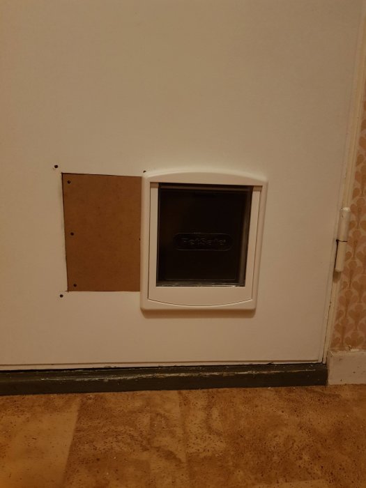 Kattlucka installerad i en vit dörr, ersätter äldre ventilgaller, inne i ett hem.