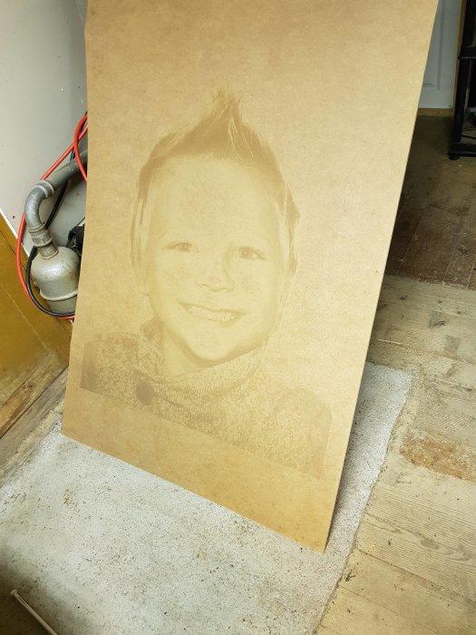 Lasergraverad bild på en MDF-skiva som visar ett porträtt av ett leende barn.