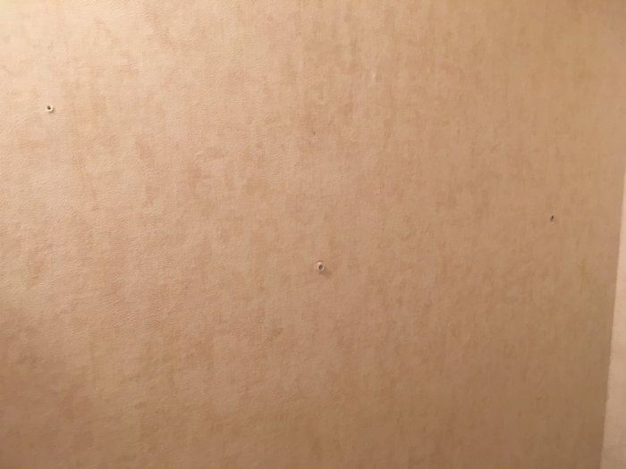 Vägg med våtrumsmatta och synliga borrhål som ska renoveras.
