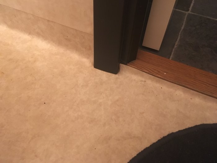 Golv med våtrumsmatta i anslutning till en dörrtröskel och svarta klinkerplattor.
