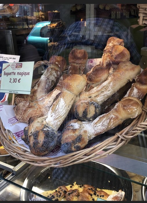Flerradiga baguetter i en korg bakom ett butiksfönster med prislappen "Baguette magique, 2,30 €".