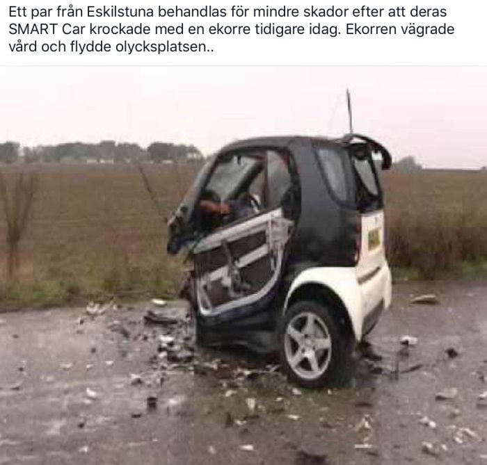Smart bil krockad på en väg med skador på kaross och framruta, vrakdelar spridda runtomkring.