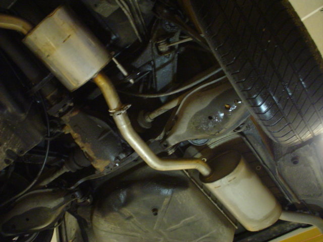 Undersidan av en bil med rostfritt Ferrita avgassystem som är i gott skick, omgiven av äldre bilkomponenter.