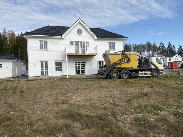 Borrfirma lastbil framför vitt hus med svart tak, klart för arbete med energibrunn.