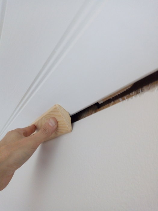 Hand håller en snedskuren trälist mot en vägg och snettak där listens vinkel inte matchar.
