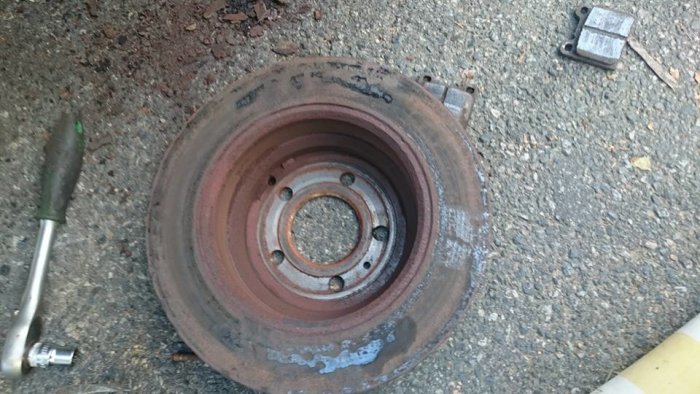 En rostig bromsskiva med synliga vågor i metallen, omgiven av verktyg och en gammal domkraft på gruset.