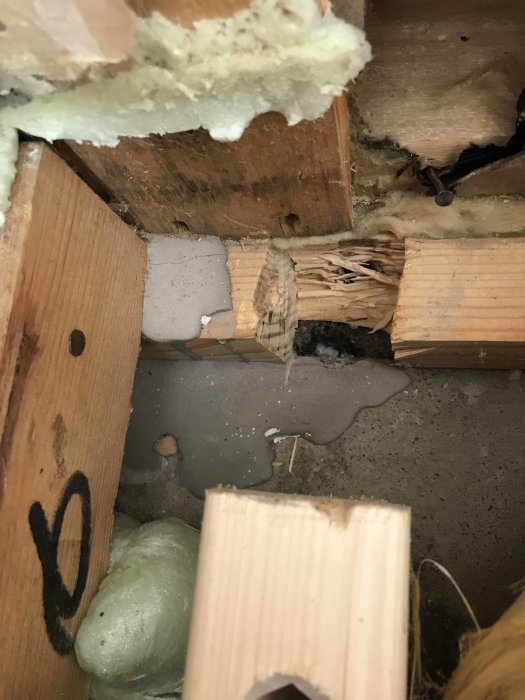 Skadad träsyll med mörk färgton intill ett ljusare träelement och isolering, indikerar potentiell otryckt träbehandling.