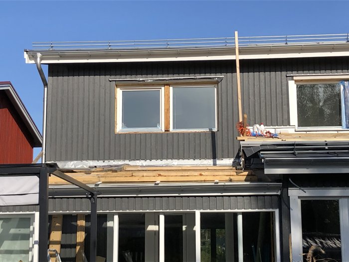 Nymålat grått hus med fönster under behandling och målarutrustning på en planka.