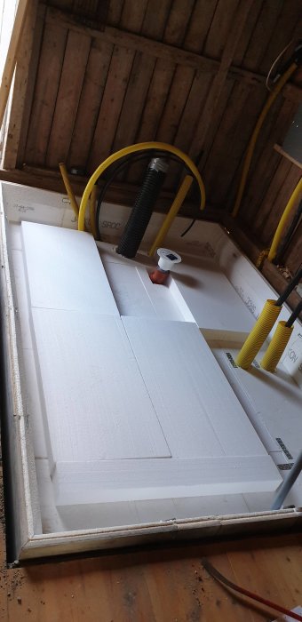 Isoleringsplattor utlagda på golv med gula slangar och armeringsjärn i ett pågående byggprojekt av ett rum.