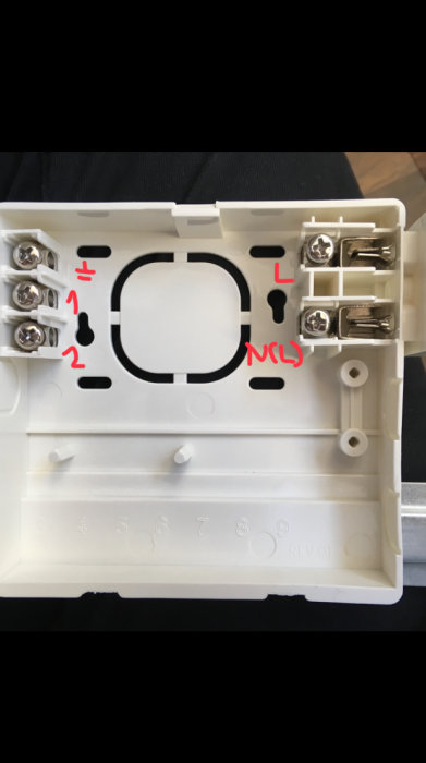 Öppnad anslutningslåda på en radiator med märkta ledningsterminaler för fas 1, fas 2 och jord, utan kablar kopplade.