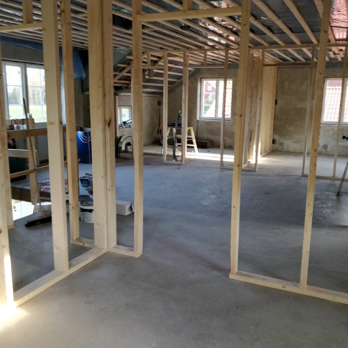 Renoveringsprojekt med nyuppförda träreglar för väggar på en betonggrund i ett tomt rum, verktyg syns i bakgrunden.