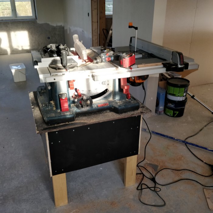 Nyinstallerad Triton-fräs i bordssåg på en hemmagjord arbetsbänk i ett under-renovering hus.