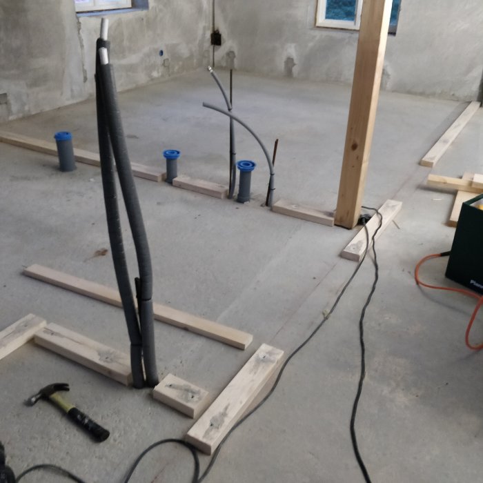 Nykonstruerade regelväggar och installationer på ett rått betonggolv i ett hus under uppbyggnad.