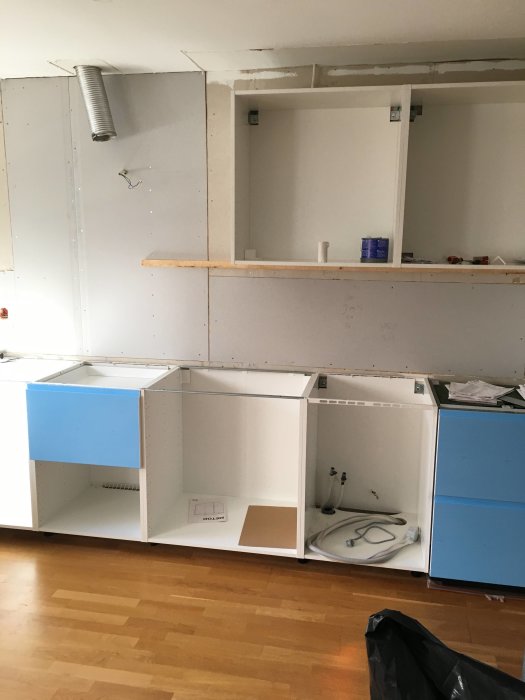 Pågående renovering av kök med montering av nya vita skåpstommar och blå lådfronter.