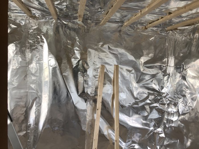 Uppspänd aluminiumfolie på bastuväggar och tak, lagad med tejp, med synliga träläkter.