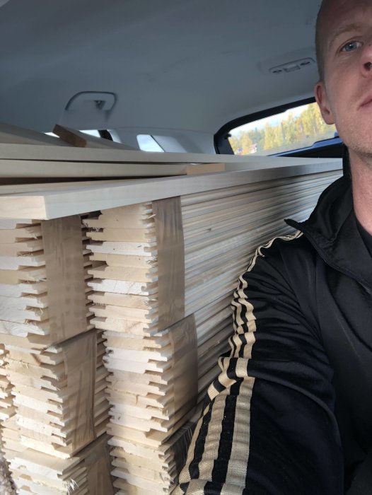 Man tar selfie med en last av uppsågad bastupanel i längder i bilens bagageutrymme.