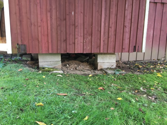 Bottendel av en bod höjd med betongblock, synligt skräp och gräs i förgrunden.