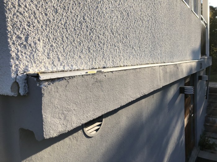Del av husvägg med skada där puts har spruckit vid ett fönsterhörn och en ventils utgång.