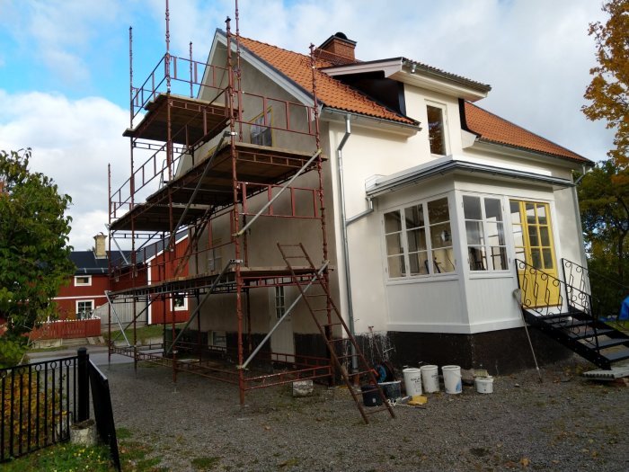 Hus med byggnadsställning och hinkar redo för vitkalkning av fasaden.