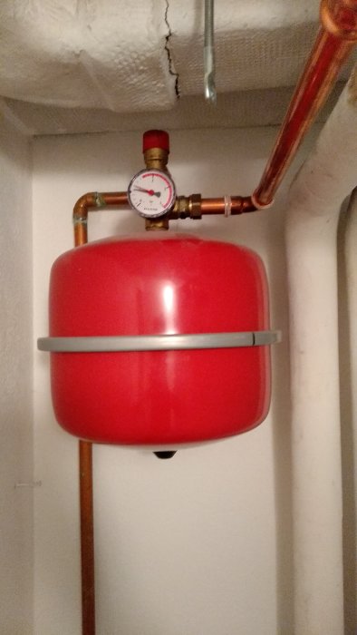 Expansionskärl med manometer i ett värmesystem, rörledningar och en ventilkran syns.