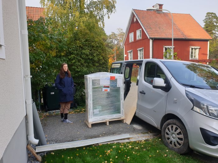 Person står bredvid en lastad pall med fönster lutad mot en skåpbil utomhus.